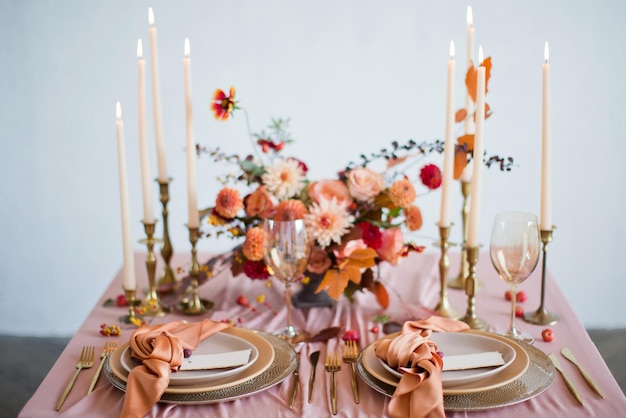 Schöne Tischdekoration mit Herbstblumen, orangefarbenen und rosafarbenen Servietten und brennenden Kerzen