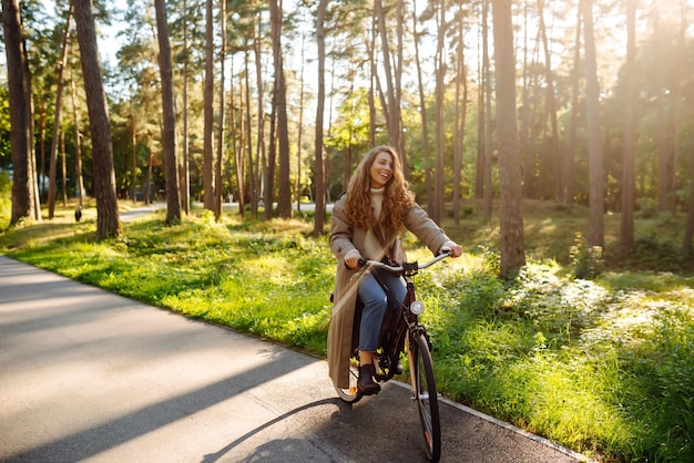 Schöne Touristin mit Locken im Mantel fährt Fahrrad, genießt das Frühlingswetter, aktiver Lebensstil