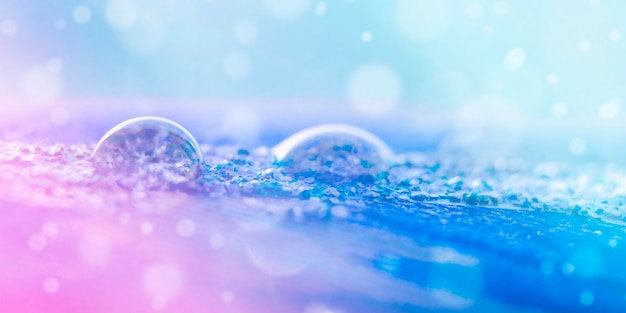 Schöne transparente Wassertropfen auf einer Feder in Rosa- und Blautönen im Sonnenlicht mit Bokeh