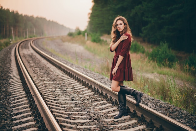 Schöne traurige nachdenkliche Frau mit lockigem natürlichem Haar auf Natur im Wald auf Eisenbahn.