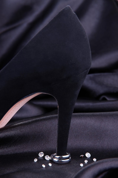 Schöne Trauringe an der Ferse des schwarzen weiblichen Schuhs, auf Seidenhintergrund