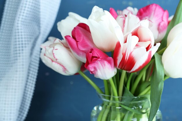 Schöne Tulpen im Glaskrug auf farbigem Holzhintergrund