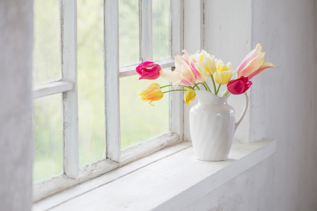 Schöne Tulpen in Vase auf weißem Fensterbrett