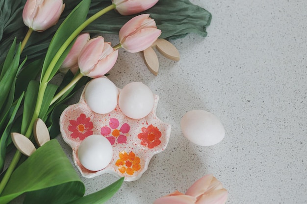 Schöne Tulpen natürliche Eier und Hasendekoration auf modernem Tisch Stilvolle Osterwohnung lag mit Kopierraum Fröhliche Ostern Handgemachte Eierhalter rosa Tulpen und Hasenohren aus Holz