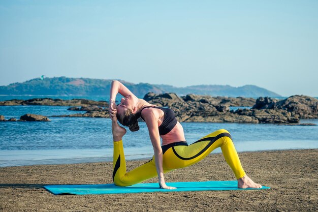 Schöne und flexible Stürmerin, die Yoga praktiziert und Dehnübungen für den Strand macht