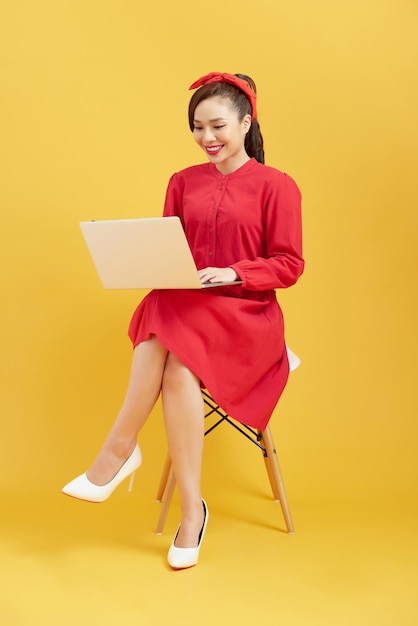 Schöne und glückliche Frau, die mit einem Laptop arbeitet, der über gelbem Hintergrund isoliert ist