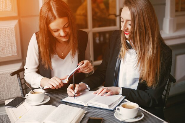 schöne und stilvolle junge Geschäftsfrauen, die in einem Café und in einem Arbeiten sitzen