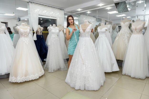 Schöne Verkäuferin, die Hochzeitskleid auf Schaufensterpuppe misst