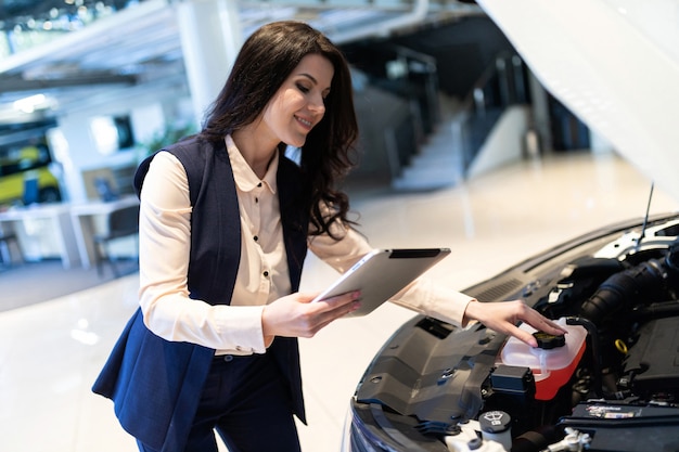 Schöne Verkaufsmanager inspizieren neues Auto mit Hilfe des Tablets im Verkaufszentrum