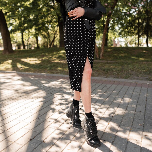 Schöne weibliche Beine in modischen schwarzen Lederstiefeln an einem sonnigen Frühlingstag. hübsches Mädchen in einem modischen schwarzen Kleid und Schuhen geht im Park spazieren