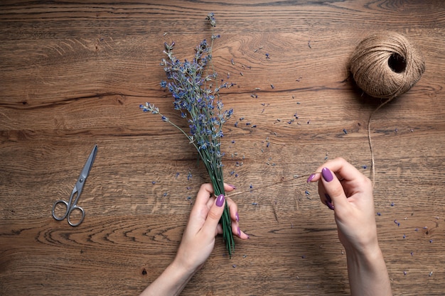 Schöne weibliche Hände binden einen Haufen trockener Lavendel auf dem Hintergrund der Eichentisch-Draufsicht