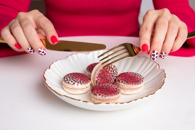 Foto schöne weibliche hände mit mode-maniküre, nägeln mit leoparden-design, die eine gabel halten und macarons essen