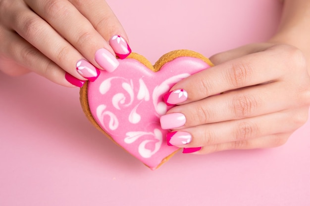 Schöne weibliche Hände mit rosa Maniküre-Nägeln, Blumendesign, Süßigkeiten in Form von Herzen halten