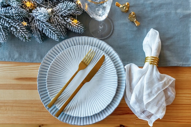 Schöne Weihnachtstischdekoration auf Holztisch. Festliches Gedeck für Weihnachtsessen in goldener und blauer Farbe. Ansicht von oben.