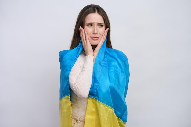 Schöne weinende ukrainische junge Frau, eingehüllt in die ukrainische Flagge isoliert auf weißem Hintergrund