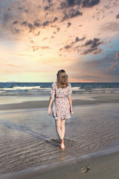 Schöne weißrussische Frau, die am Strand gegen einen dramatischen und romantischen Himmel spazieren geht