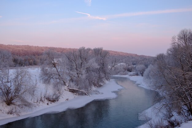 Schöne Winterlandschaft mit Blick auf den gewundenen Fluss bei Sonnenaufgang und Schneebänken