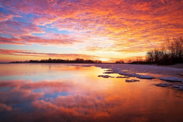 Schöne Winterlandschaft mit feurigem Himmel des Sonnenuntergangs und gefrorenem See. Zusammensetzung der Natur.