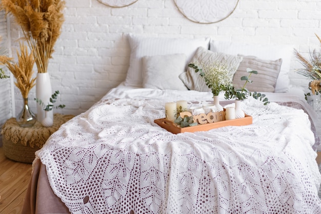 Schöne Wohneinrichtung in Weiß- und Beigetönen, mit Traumfängern, Trockenblumen und einem Bett. Interieur eines gemütlichen Hauses