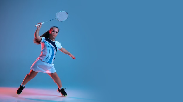 Schöne Zwergfrau, die im Badminton übt, lokalisiert auf blauem Hintergrund im Neonlicht