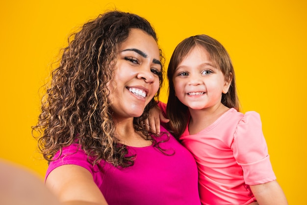 Schönen Muttertag! Entzückendes kaukasisches Kind mit seiner Mutter, die selfie auf gelbem Hintergrund macht.