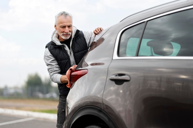 Schöner älterer männlicher Fahrer, der sein Auto mit Freude wie ein erfahrenes Personal wäscht und poliert