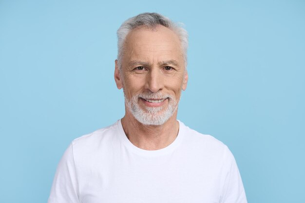 Foto schöner älterer mann, der breit lächelt und isoliert auf blauem hintergrund in die kamera blickt