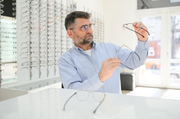 Schöner älterer Mann, der Brillengestell im Optikgeschäft auswählt