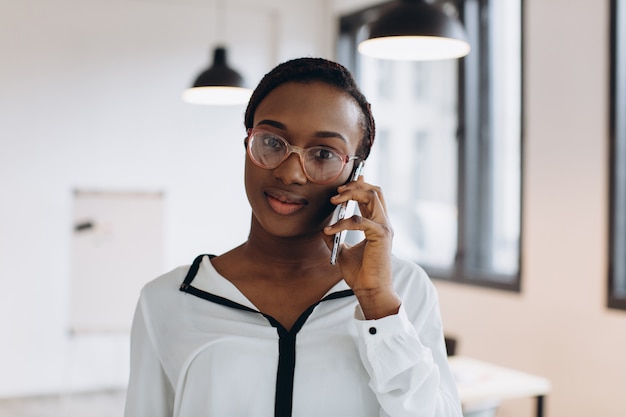 Schöner afrikanischer Firmenarbeiter, der auf Handy in modernem Büro spricht