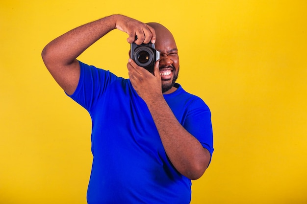 Schöner afro-brasilianischer Mann mit Brille blaues Hemd über gelbem Hintergrund Fotografieren mit Fotokamera Fotograf lächelnd kreative DSLR