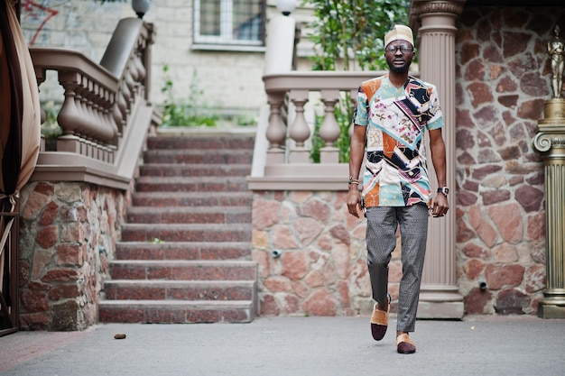 Schöner afroamerikanischer Mann mit traditioneller Kleiderkappe und Brille in der modernen Stadt