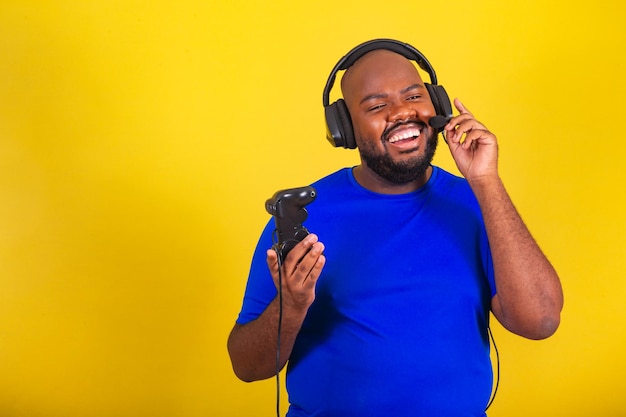 Schöner afrobrasilianischer Mann mit Brille blaues Hemd über gelbem Hintergrund Spielen mit Freunden Multiplayer-Gamer interagieren mit Sprachanruf-Spielen Unterhaltung