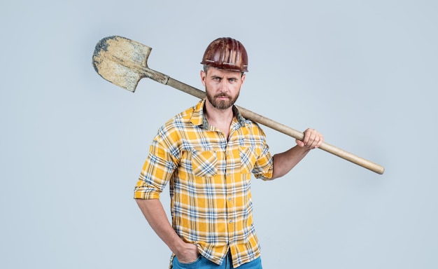 Schöner Arbeiter mit Bauschutzhelm und kariertem Hemd auf der Baustelle mit Schaufelindustrie