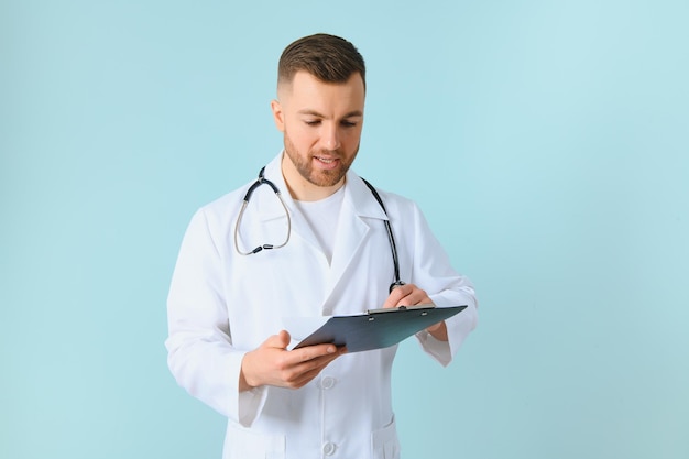 Schöner Arzt mit Mantel und Stethoskop vor isoliertem blauem Hintergrund