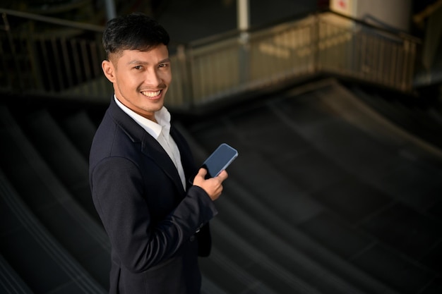 Schöner asiatischer Geschäftsmann, der sein Smartphone hält, während er die Treppe in einer Stadt hinuntergeht