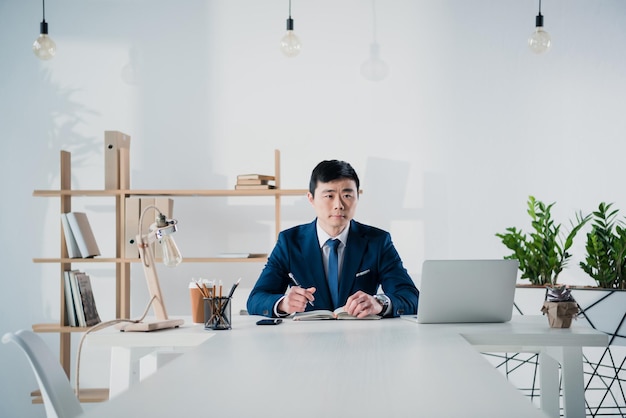 Schöner asiatischer Geschäftsmann mit Laptop am Arbeitsplatz