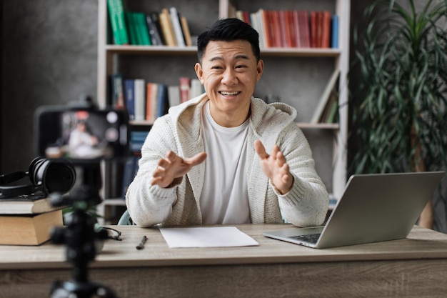 Schöner asiatischer Mann in Freizeitkleidung, der spricht und gestikuliert, während er Videos auf einem modernen Telefon aufnimmt