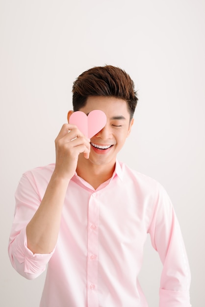 Schöner asiatischer Mann mit rosa Herzpapier posiert auf grauem Hintergrund