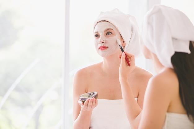 Schöner Badekurort der jungen Frau und des Freunds, der kosmetische Maskencreme auf dem Gesicht sich entspannt empfängt Massage anwendet
