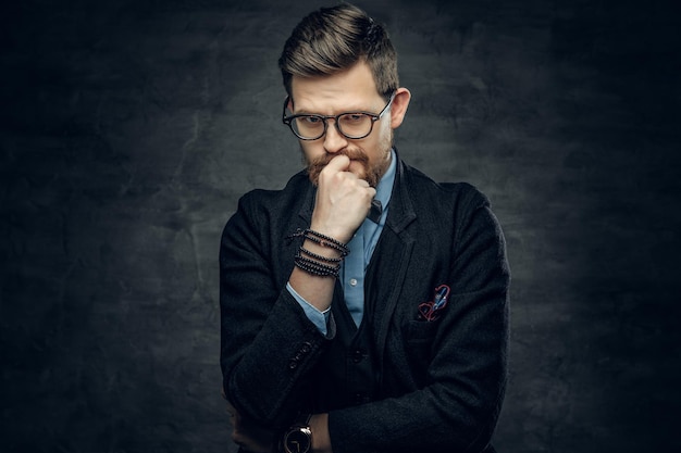 Schöner bärtiger, eleganter mann mit brille, gekleidet in einen dunkelblauen anzug mit fliege über grauem vignettenhintergrund.