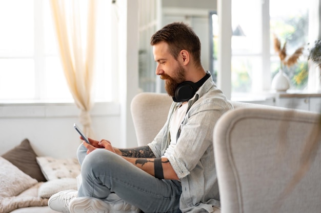 Schöner bärtiger Mann mit digitalem Tablet, während er sich zu Hause auf der Couch ausruht