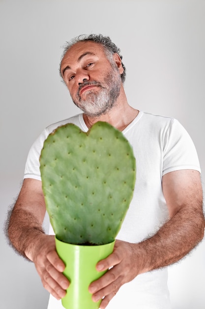 Schöner bärtiger reifer Mann hält einen herzförmigen Kaktus im Topf