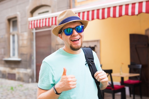 Schöner bärtiger Tourist mit Rucksack macht Reisen durch die Stadt. Mann steht und Daumen aufgibt.