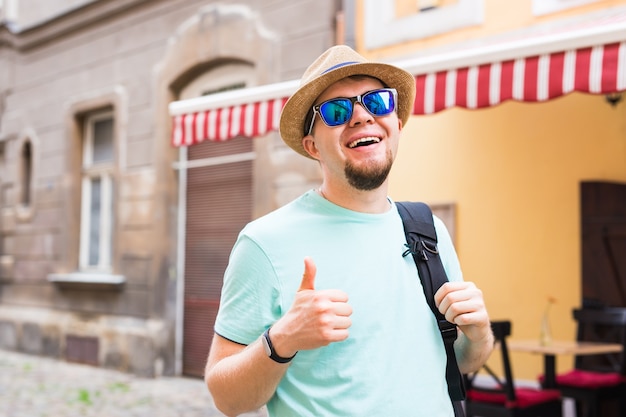 Schöner bärtiger Tourist mit Rucksack macht Reisen durch die Stadt. Mann steht und Daumen aufgibt.