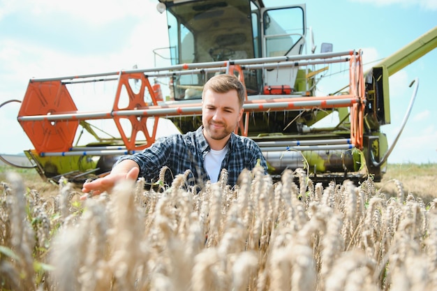 Schöner Bauer mit Tablet, der während der Ernte auf dem Feld vor dem Mähdrescher steht