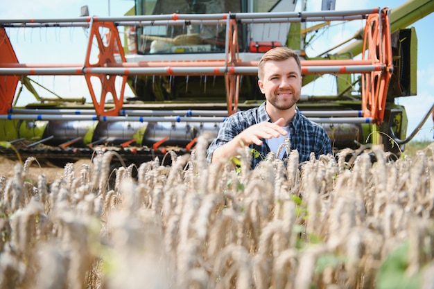 Schöner Bauer mit Tablet, der während der Ernte auf dem Feld vor dem Mähdrescher steht