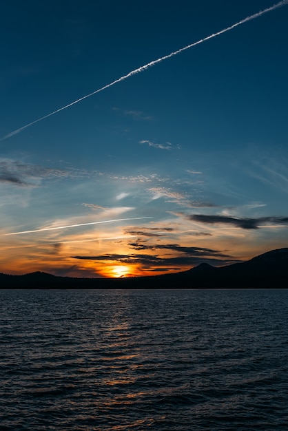 Schöner Bergsee bei Sonnenuntergang, vertikale Ansicht. Ein See zwischen den Bergen bei Sonnenuntergang. Abendlandschaft. Sonnenunterganghimmel mit dunklen Wolken und Bergen am See in der goldenen Zeit. Platz kopieren