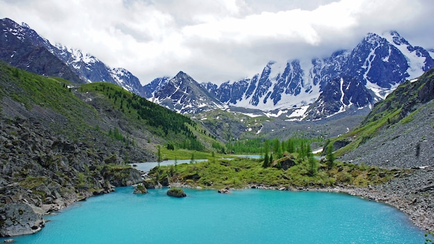 Schöner Bergsee mit türkisfarbenem klarem Wasser im Altai. Hohe mpuntains mit Schnee und Bäumen