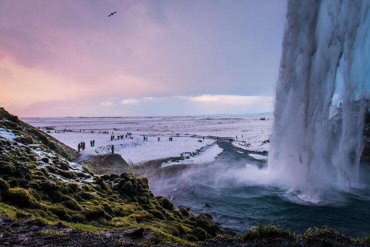 Foto schöner blick auf den wasserfall durch die schneebedeckte landschaft gegen den bewölkten himmel beim sonnenuntergang