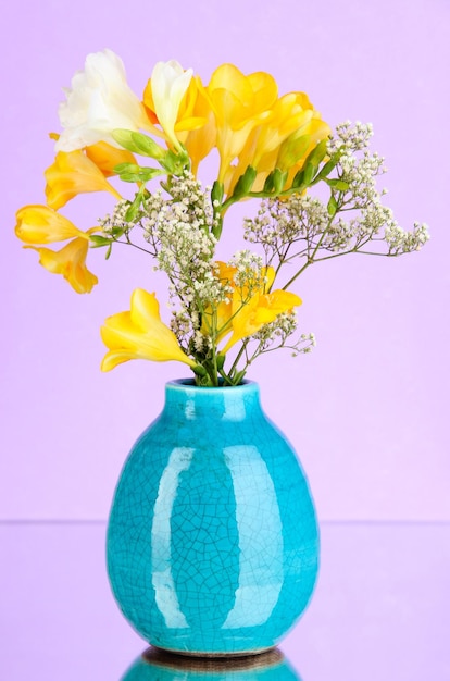 Schöner Blumenstrauß aus Freesien in Vase auf violettem Hintergrund